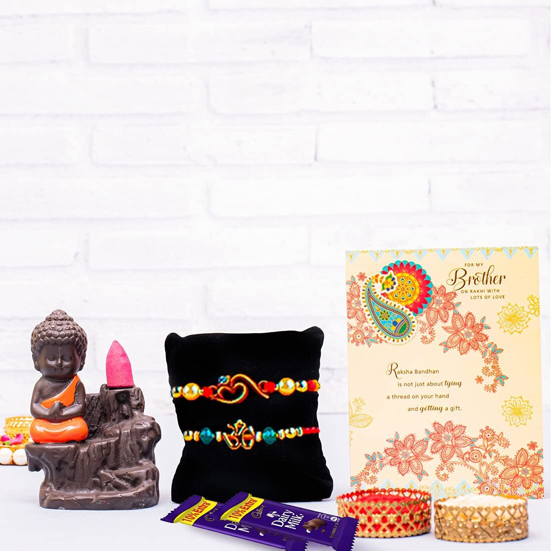 ARCHIES Rakhi for Brother Rakshabandhan Combo of 1 Nirvana Buddha Idol, 2 Auspicious Om Rakhis and 2 Dairy Milk Chocolates 13.2gm With 1 Roli & Chawal Set-10gm & Greeting Card (Pack of 7)
